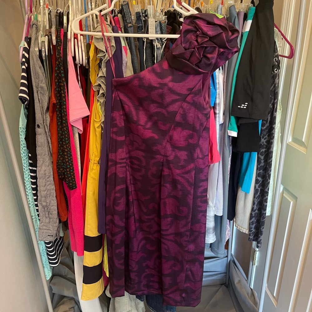 A purple party dress with a rosette on one shoulder is in perfect condition.